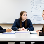 A diverse group of four young adult students, fully clothed in modest, professional student attire, are seated around a modern table in a bright, contemporary university study lounge. They are deeply engaged in a focused discussion, with one student pointing to a complex diagram on a whiteboard, illustrating concepts of public administration and legal frameworks. The scene reflects deep understanding and collaborative learning. Soft, diffused lighting, high-resolution, professional photography, perfect anatomy, correct proportions, natural pose, well-formed hands, proper finger count, natural body proportions, safe for work, appropriate content, family-friendly, fully clothed.